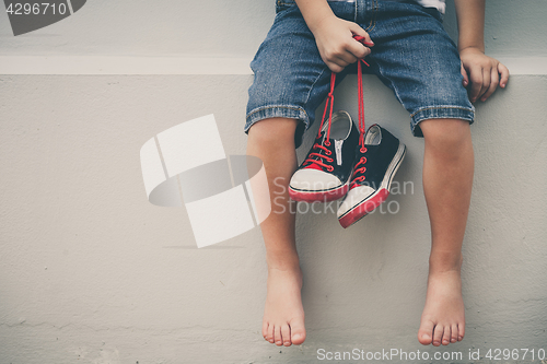 Image of Little boy  sitting near the house and keeping the youth sneaker