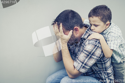 Image of sad son hugging his dad near wall