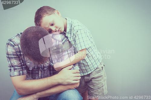 Image of sad son hugging his dad near wall