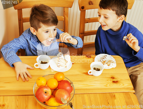 Image of little cute boys eating dessert on wooden kitchen. home interior