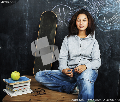 Image of young cute teenage girl in classroom at blackboard seating on ta