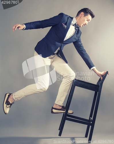 Image of young handsoman businessman fooling aroung with chair, modern mem