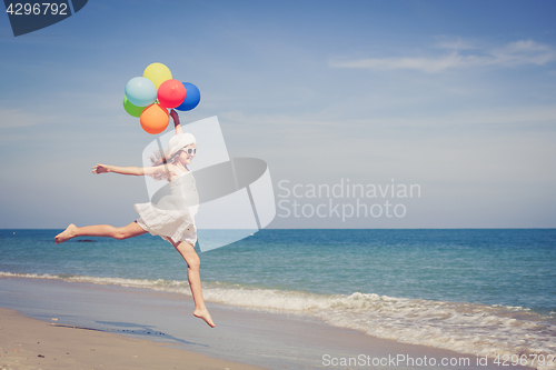 Image of Teen girl with balloons jumping on the beach