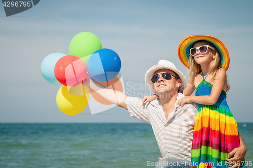 Image of Father and daughter with balloons playing on the beach at the da