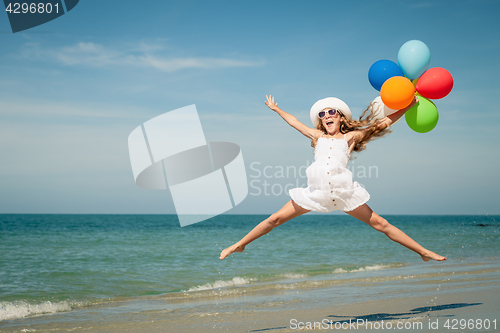 Image of Teen girl with balloons jumping on the beach