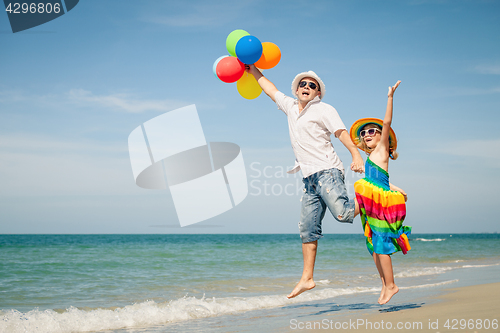 Image of Father and daughter with balloons playing on the beach at the da