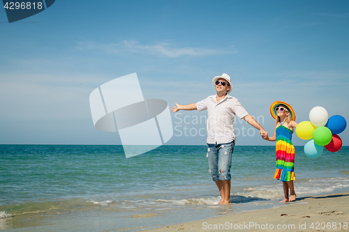 Image of Father and daughter with balloons playing on the beach at the da