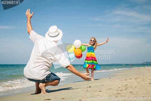 Image of Father and daughter with balloons playing on the beach at the da