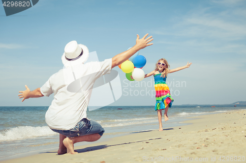 Image of Father and daughter with balloons playing on the beach at the da