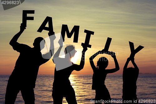 Image of Happy family standing on the beach at the sunset time. 