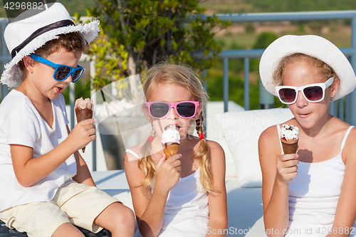 Image of Three happy children eating ice cream near swimming pool at the 