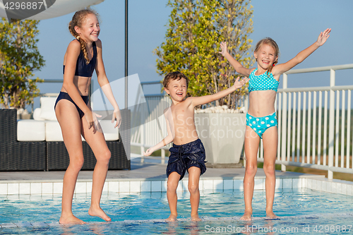 Image of Three happy children playing on the swimming pool at the day tim