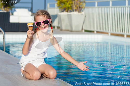 Image of happy little girl with ice cream sitting near a swimming pool at