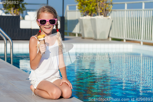 Image of happy little girl with ice cream sitting near a swimming pool at