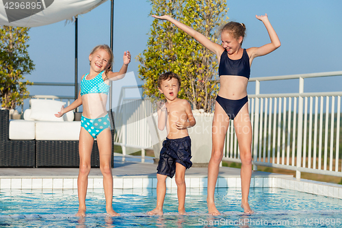 Image of Three happy children playing on the swimming pool at the day tim