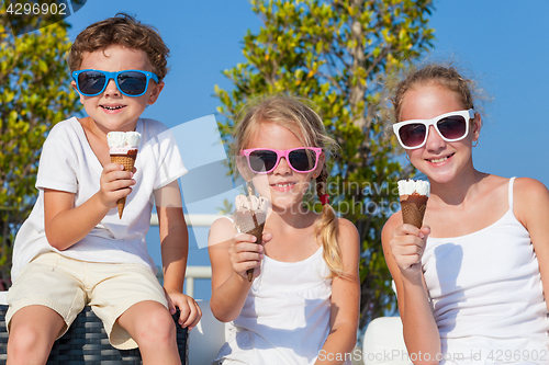 Image of Three happy children eating ice cream near swimming pool at the 