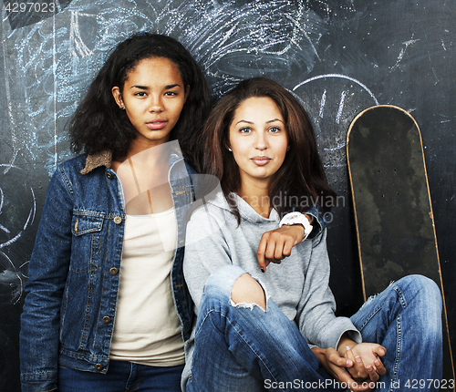 Image of back to school after summer vacations, two teen real girls in classroom with blackboard painted together, lifestyle mixed races people concept 