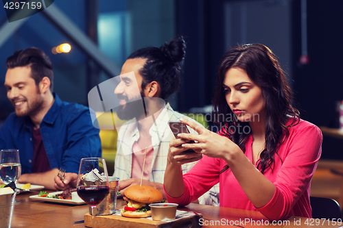 Image of woman with smartphone and friends at restaurant