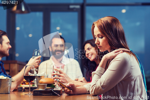Image of woman with smartphone and friends at restaurant