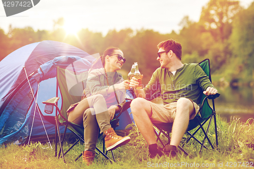 Image of happy couple clinking drinks at campsite tent