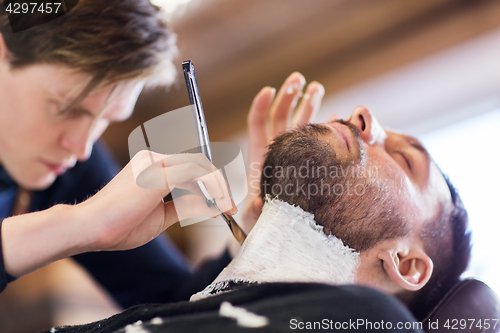 Image of man and barber with straight razor shaving beard