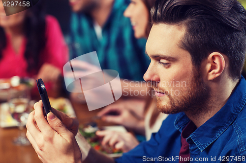 Image of man with smartphone and friends at restaurant