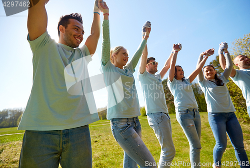 Image of group of happy volunteers holding hands outdoors