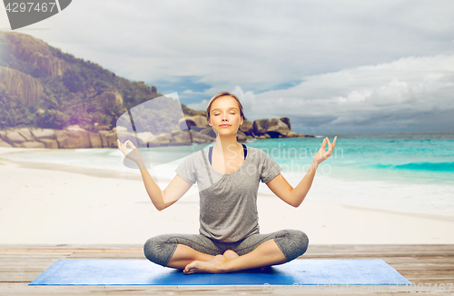 Image of woman doing yoga meditation in lotus pose on beach