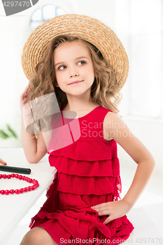 Image of A little girl with cosmetics. She is in mother\'s bedroom, sitting near the mirror.