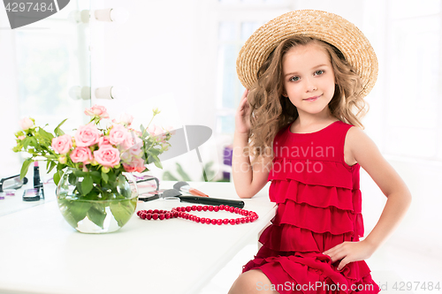 Image of A little girl with cosmetics. She is in mother\'s bedroom, sitting near the mirror.