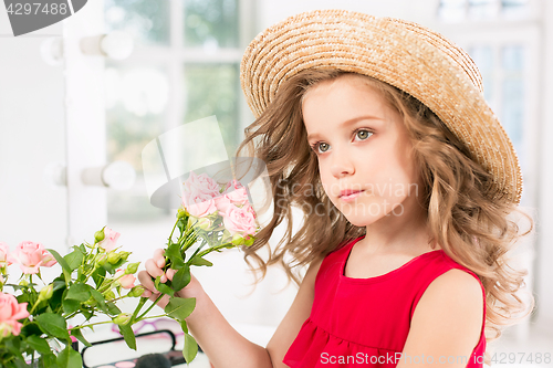 Image of A little girl with roses. She is in mother\'s bedroom, sitting near the mirror.
