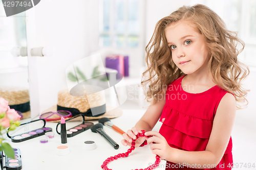 Image of A little girl with cosmetics. She is in mother\'s bedroom, sitting near the mirror.