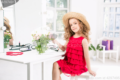 Image of A little girl with cosmetics. She is in mother\'s bedroom, sitting near the mirror.