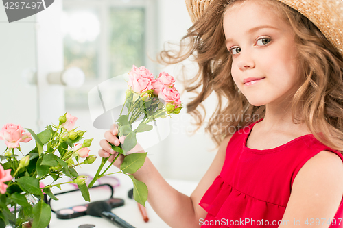 Image of A little girl with roses. She is in mother\'s bedroom, sitting near the mirror.