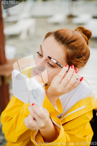 Image of Woman doing makeup outside