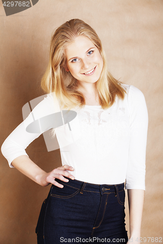 Image of young cool blong teenage girl messed with her hair smiling close up on warm brown background, lifestyle people concept