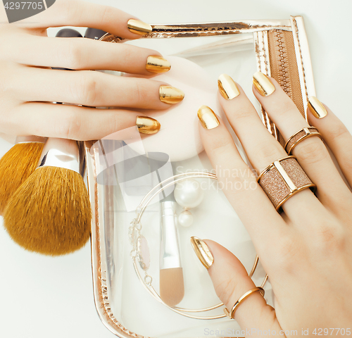 Image of woman hands with golden manicure and many rings holding brushes, makeup artist stuff stylish, pure close up pink flower rose tenderness among cosmetic