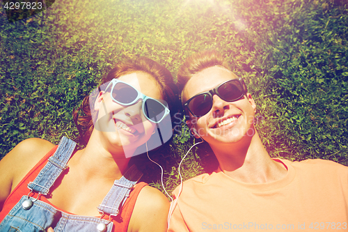 Image of happy teenage couple with earphones lying on grass