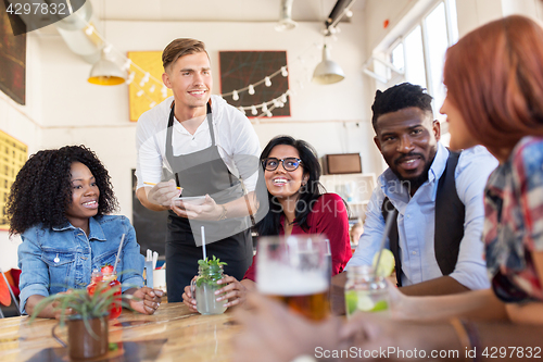 Image of waiter and friends with menu and drinks at bar