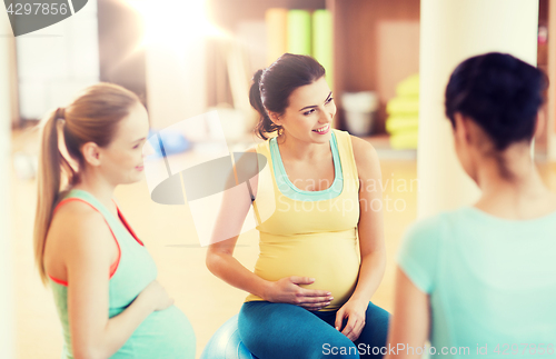 Image of happy pregnant women sitting on balls in gym