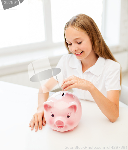 Image of happy smiling girl putting coin into piggy bank