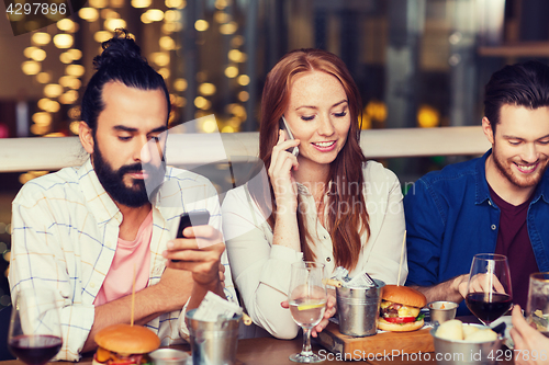 Image of happy friends with smartphones at restaurant