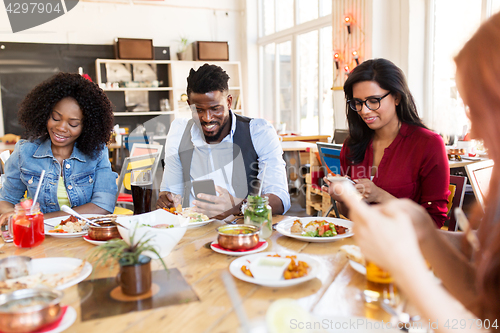 Image of happy friends with smartphones at restaurant