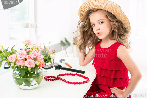 Image of A little girl with cosmetics. She is in mother\'s bedroom, sitting near the mirror.