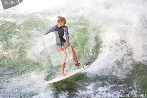 Image of Atractive sporty girl surfing on famous artificial river wave in Englischer garten, Munich, Germany.