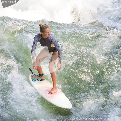 Image of Atractive sporty girl surfing on famous artificial river wave in Englischer garten, Munich, Germany.