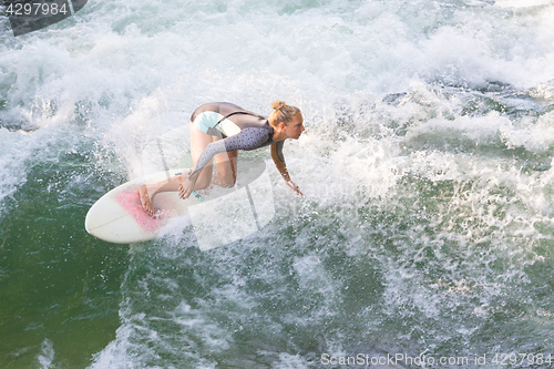 Image of Atractive sporty girl surfing on famous artificial river wave in Englischer garten, Munich, Germany.