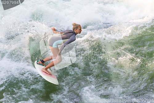 Image of Atractive sporty girl surfing on famous artificial river wave in Englischer garten, Munich, Germany.