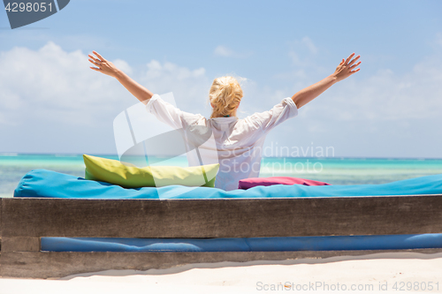 Image of Relaxed woman in luxury lounger, arms rised, enjoying summer vacations on beautiful beach.