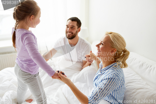 Image of happy family holding hands in bed at home